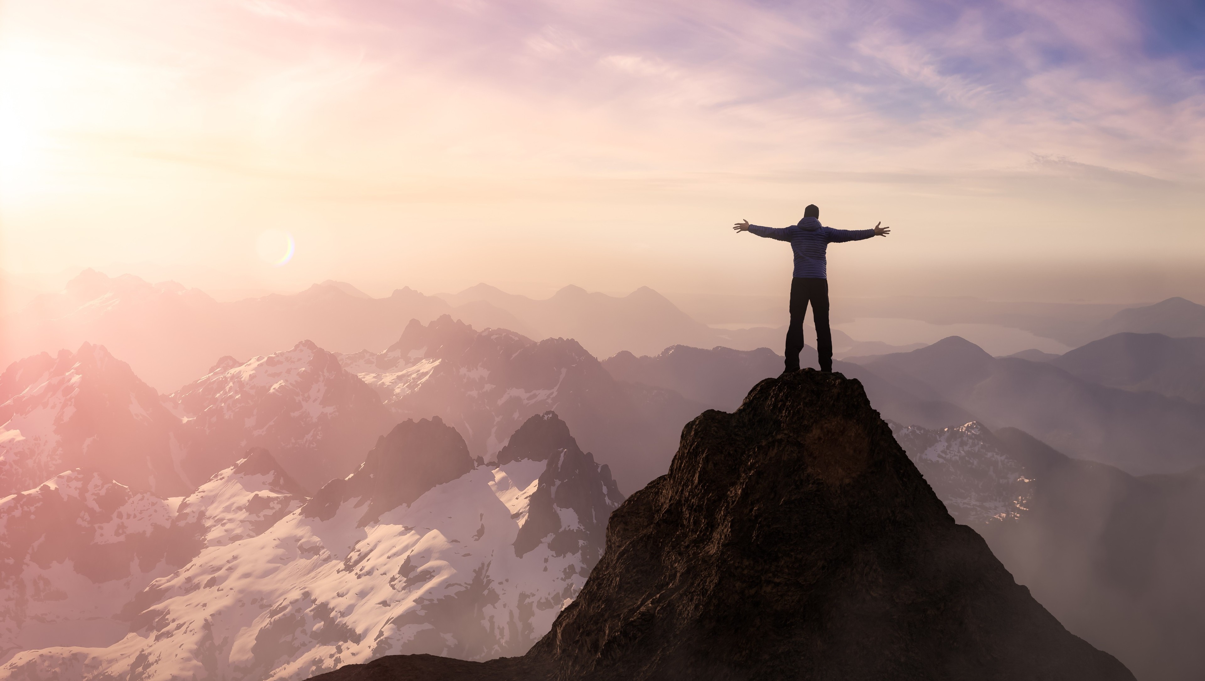 person on top of mountain peak with arms wide open in celebration